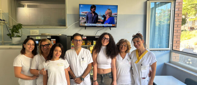 Alessandra Colacarlo con sei operatori dell'ospedale di comunità di Casoli davanti al televisore donato, appeso alla parete della zona ristoro