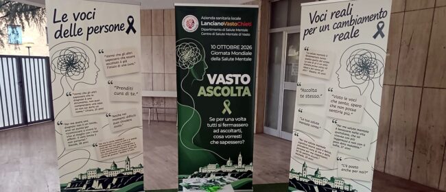 Allestimento di «Vasto ascolta» con tre roll-up, una poltrona bianca e un cubo con pieghevoli e nastri verdi.